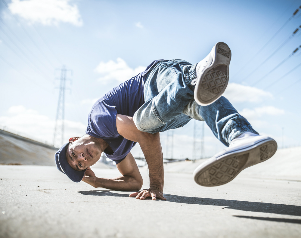 Breakdancer doing a trick on a concrete parking lot with hydro lines in the background