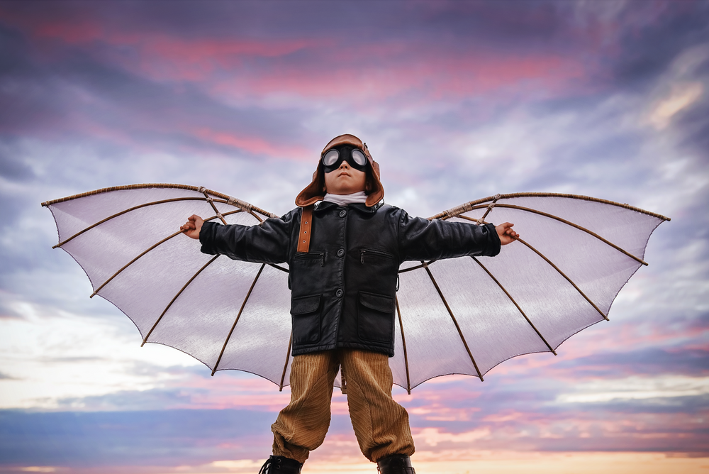 Image of a boy wearing wings and aviation glasses in front of a sunset 