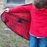 Young boy showing the inside of his Great Pretenders cape with a red background, black spider web and black spider