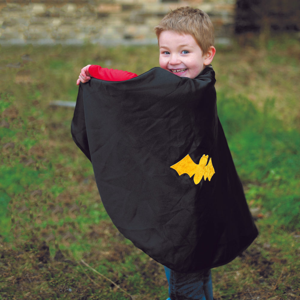 Young boy wearing a Great Pretenders black cape with a gold bat image on it