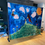 metal stand with backdrop sheet with a children's drawing of a sky and birds on it