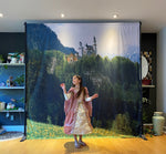 Young girl in  a princess costume in front of a banner of a castle and forest.